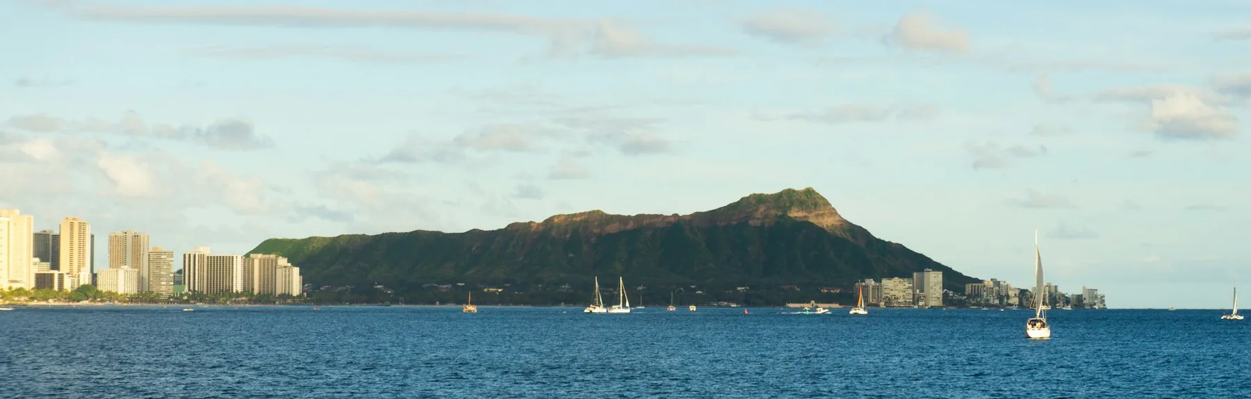 Diamond Head and the Waikiki skyline across blue water, with sailboats in the distance