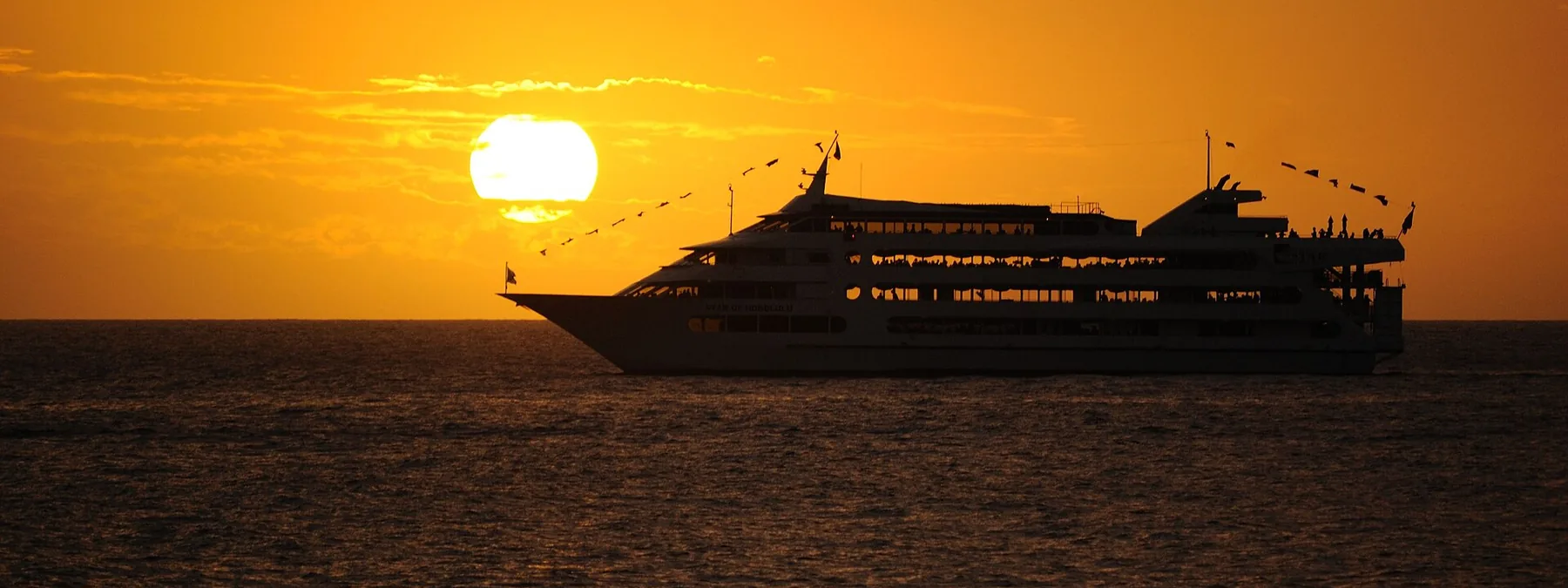 The Star of Honolulu in dark silhouette against an orange sunset with the sun low over the sea